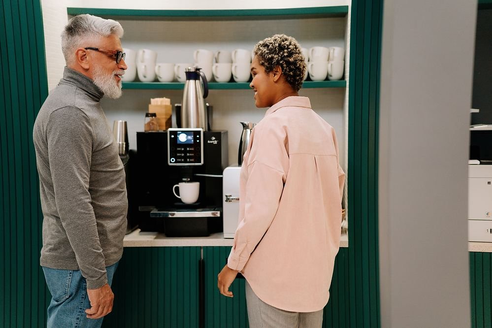 Two colleagues talking beside an office coffee machine