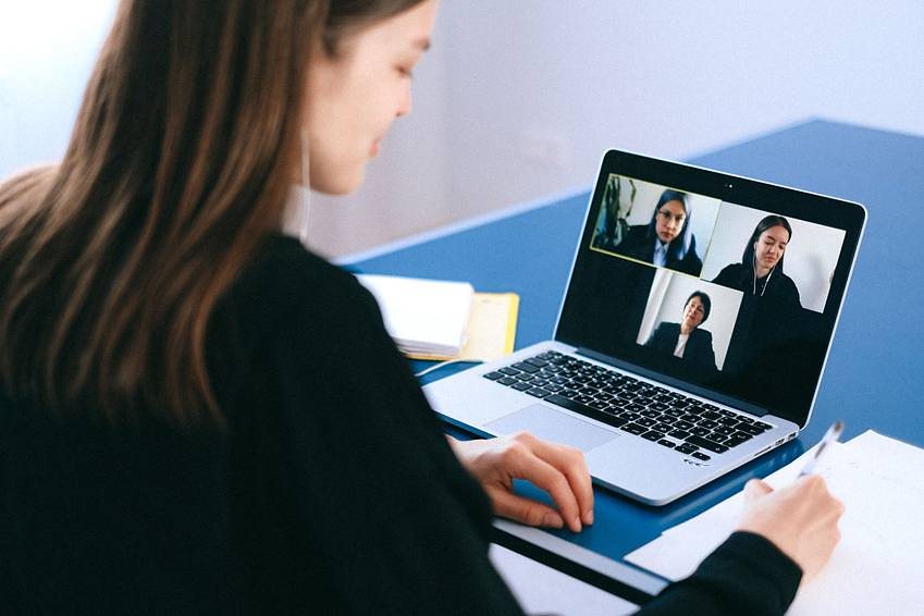A job seeker taking notes during an online session, a video call open on the laptop